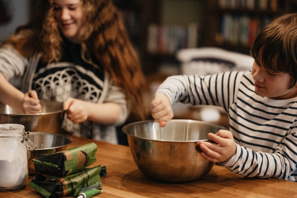 Sister and brother, working together to mix the ingredients of something they're helping to cook or bake.